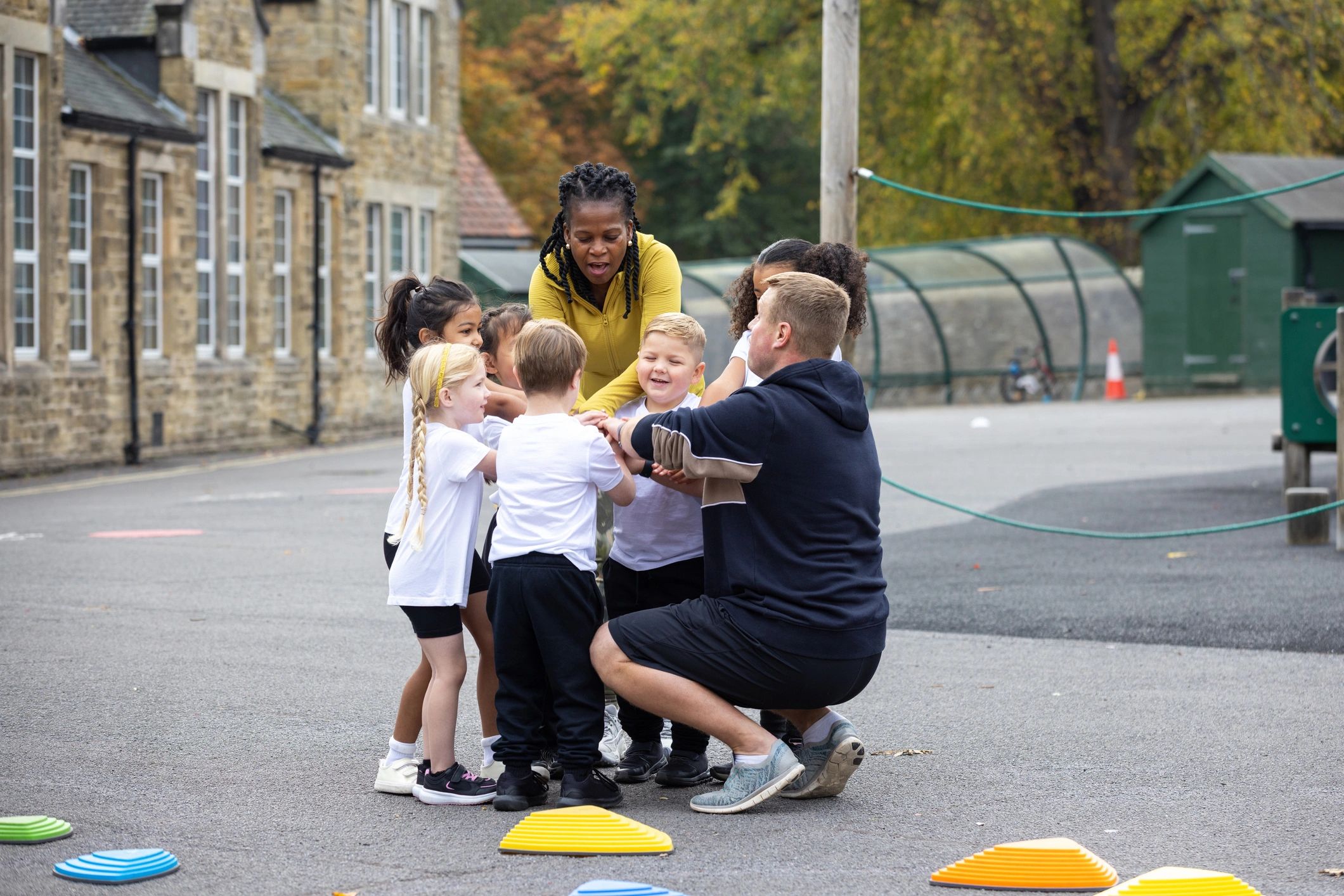 Teachers and children in a group huddle during outdoor play